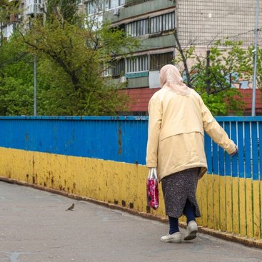 An elderly woman walks past a railing painted in yellow/blue Ukraine flag colours